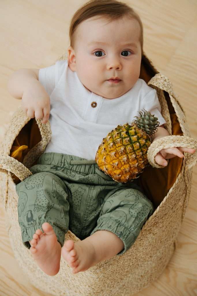baby reclines in wicker basket with a tiny pineapple